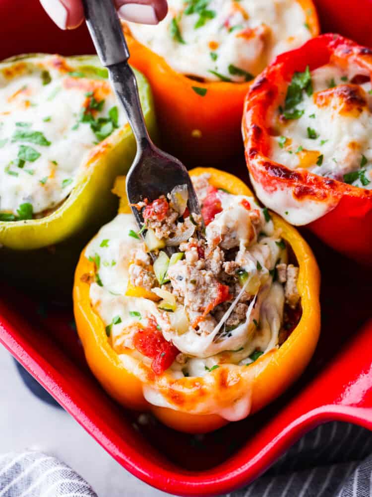 Turkey stuffed peppers combine ground turkey, tons of vegetables, and pepper jack cheese into a satisfying and healthy low-carb meal. Jumpstart your healthy eating habits with these oh-so-delicious stuffed peppers! A fork sticking into a pepper filled with ground turkey, melted cheese, and herbs.