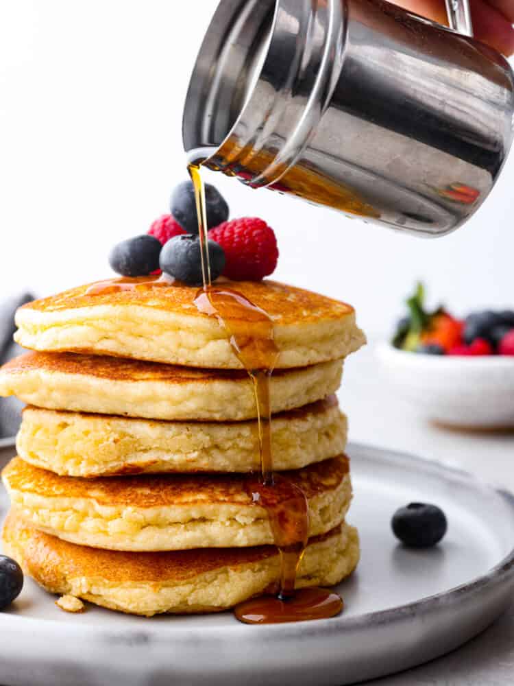 Sweet, fluffy, and keto-friendly! These delicious keto pancakes are a simple and healthy brunch option for when your craving a carb-filled breakfast but don't want to mess up your macros. Syrup being poured over a stack of 5 pancakes.