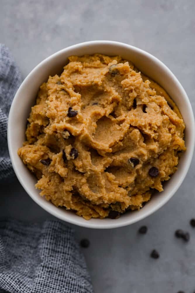 Who needs actual cookie dough when you can have chickpea cookie dough? It's the guilt-free treat that will have you feeling like a million bucks! Top-down view of cookie dough in a white bowl.