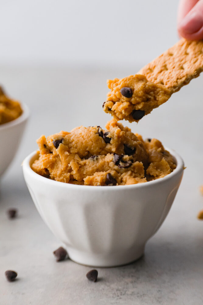 Who needs actual cookie dough when you can have chickpea cookie dough? It's the guilt-free treat that will have you feeling like a million bucks! Dipping a cracker in chickpea cookie dough.