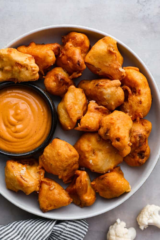 Fried cauliflower is my go-to crispy, low-carb snack that sneaks in some extra veggies and fiber. I make them for my kids all the time. They think they’re just getting a treat, but I know better! Top-down view of fried cauliflower bites served with dipping sauce.