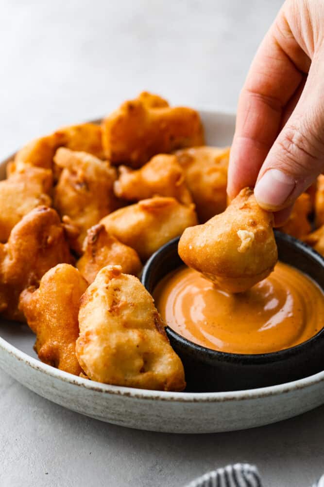 Fried cauliflower is my go-to crispy, low-carb snack that sneaks in some extra veggies and fiber. I make them for my kids all the time. They think they’re just getting a treat, but I know better! Dipping a piece of fried cauliflower into a creamy orange sauce.