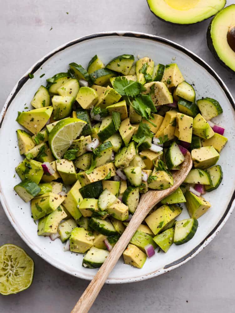 Cucumber avocado salad is the ultimate combination of creamy and crisp, tossed in a mouthwatering dressing made of lime juice, olive oil, and garlic! It's light, flavorful, and perfect for serving alongside all of your favorite summer meals. Top-down view of cucumber avocado salad in a white bowl.